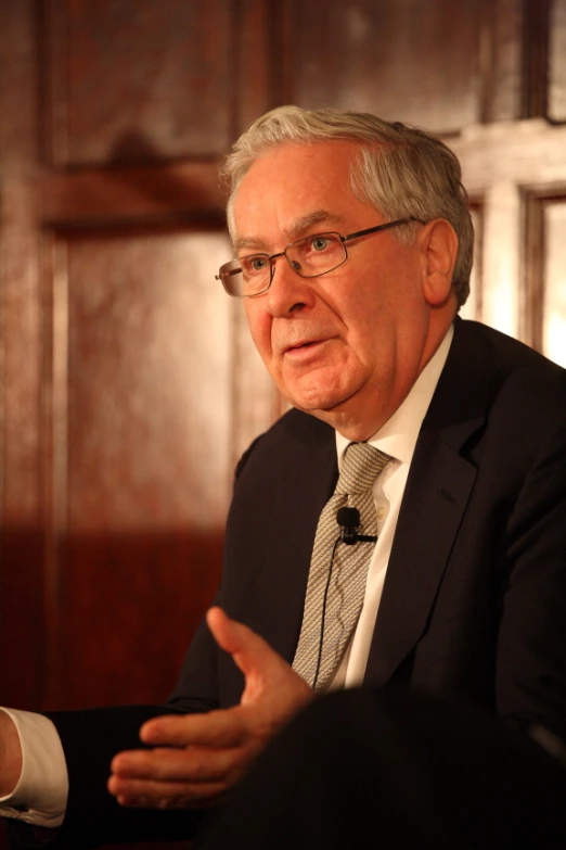 a man with glasses is speaking while wearing a suit and tie