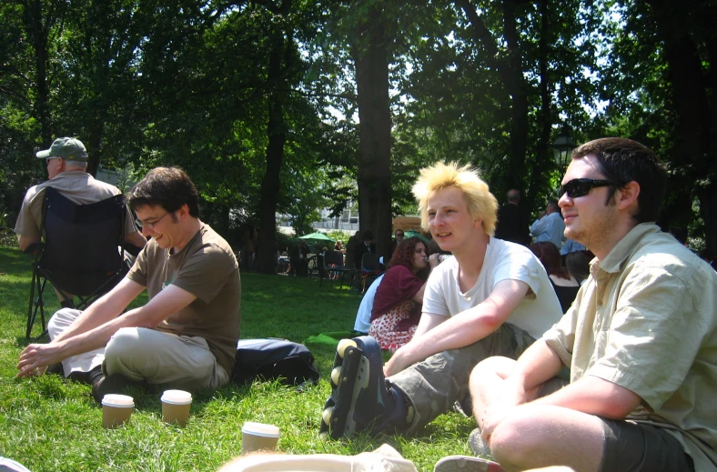 two men sitting on the grass holding cups