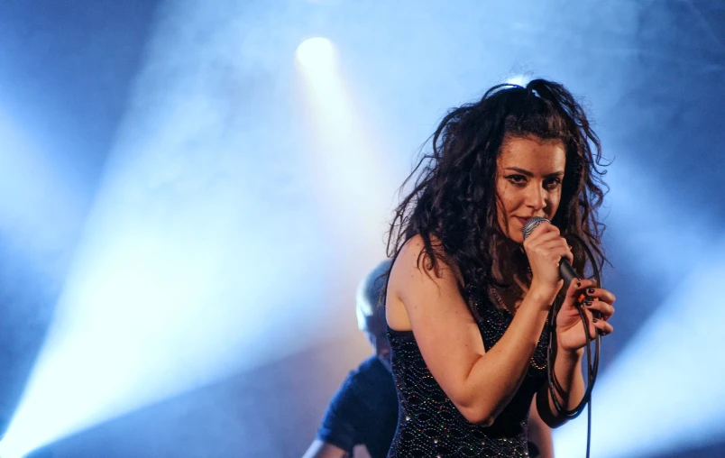 woman in dark dress performing at an event with lights from the stage