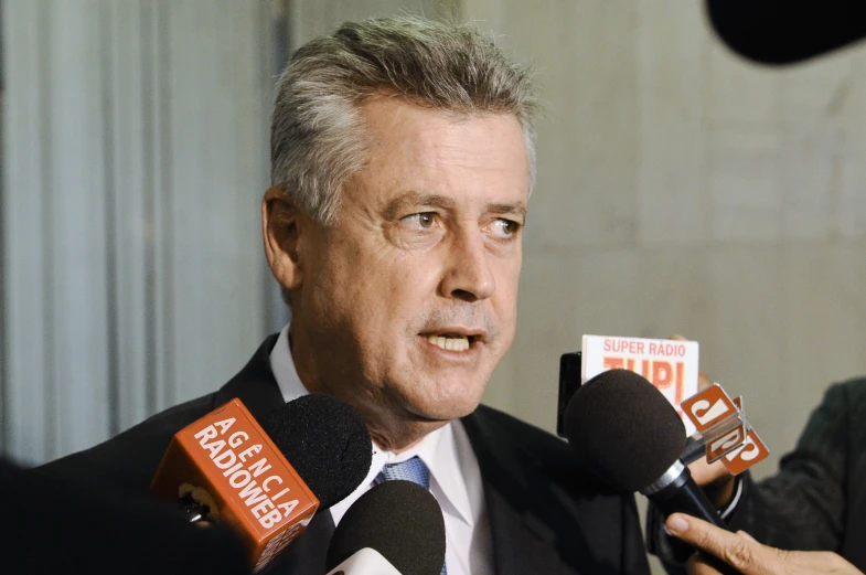 a man wearing a suit and tie talking into microphones