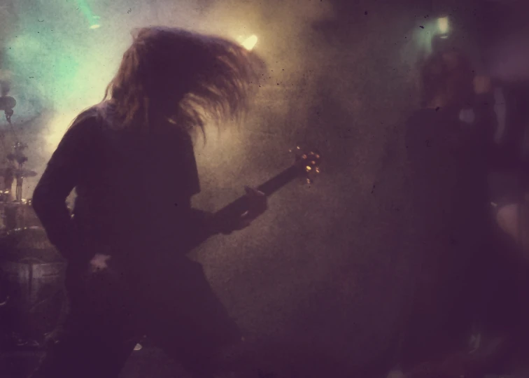 a person with long hair plays an electric guitar