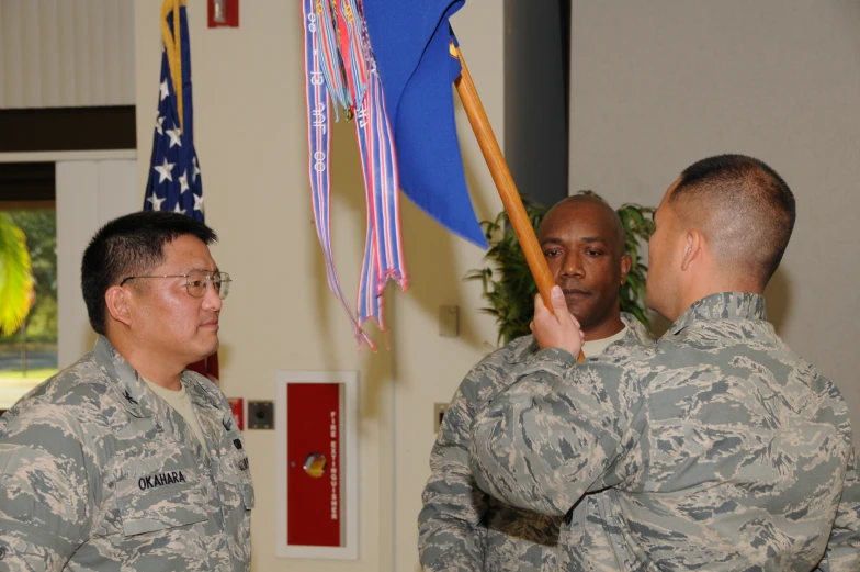 two soldiers hold flags while another man fixes an american flag