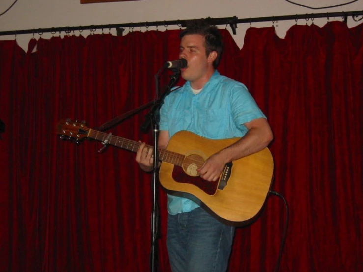 man singing into a microphone while playing an acoustic guitar