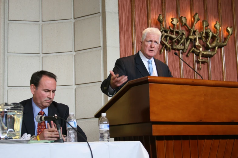 two men sitting at a podium in front of microphones