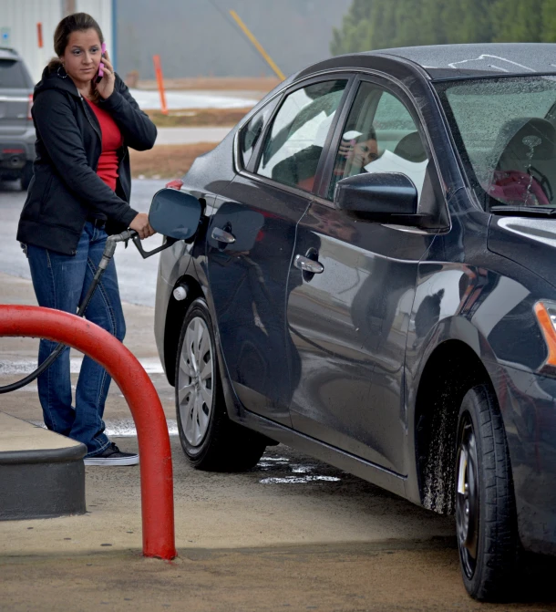 the woman is using her phone to fill up her car