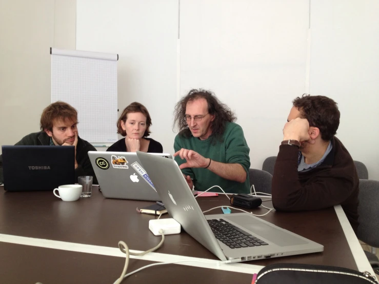 four people are sitting at a table in front of laptops