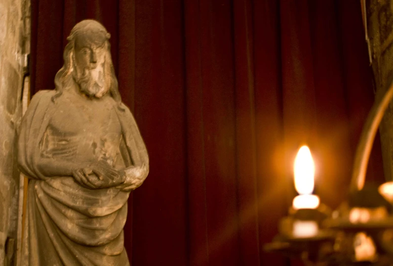 a statue of jesus holding a book next to a lit candle