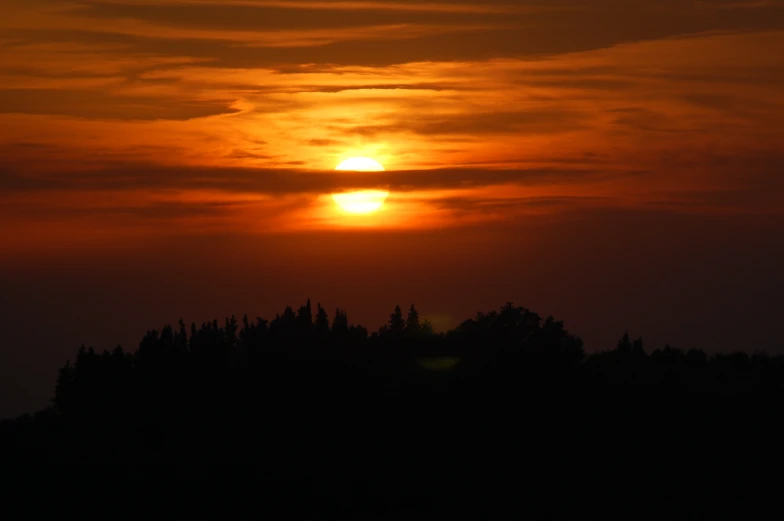 the sun sets over the top of a wooded hill