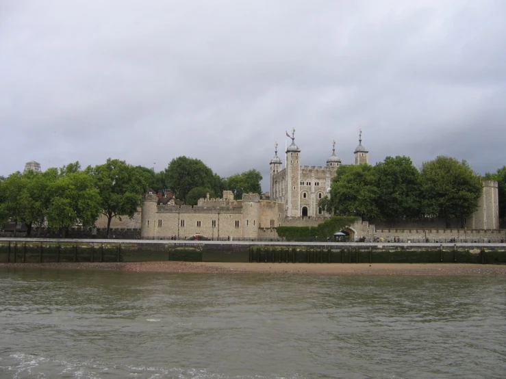 a castle stands at the edge of a river as other large buildings sit nearby