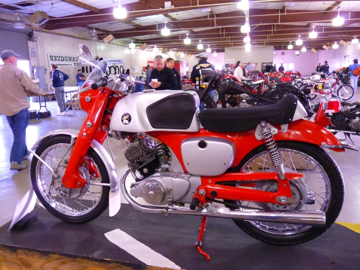 red and white motorcycle inside of a garage with people around