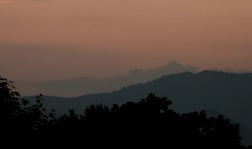 a silhouette of trees, hills and mountains are shown at sunset