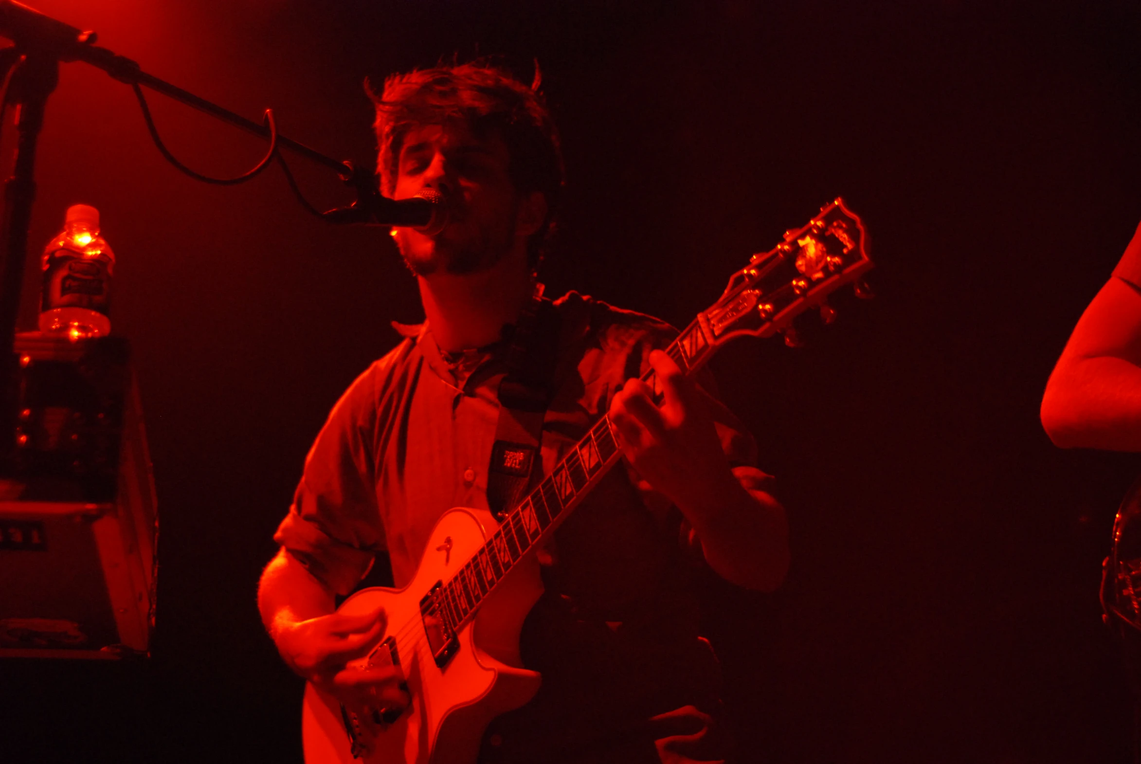 two men on stage one playing a guitar and the other singing into a microphone