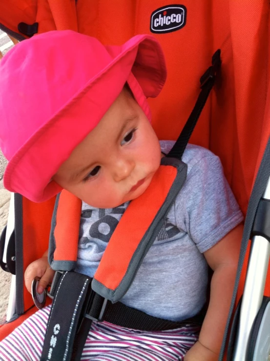 small child wearing a bright pink hat sitting in a red stroller