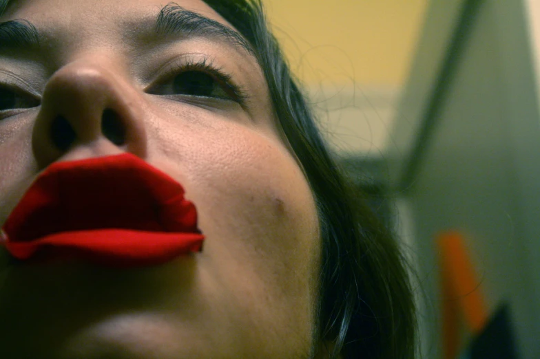 a close up of a woman with a red piece of paper on her mouth