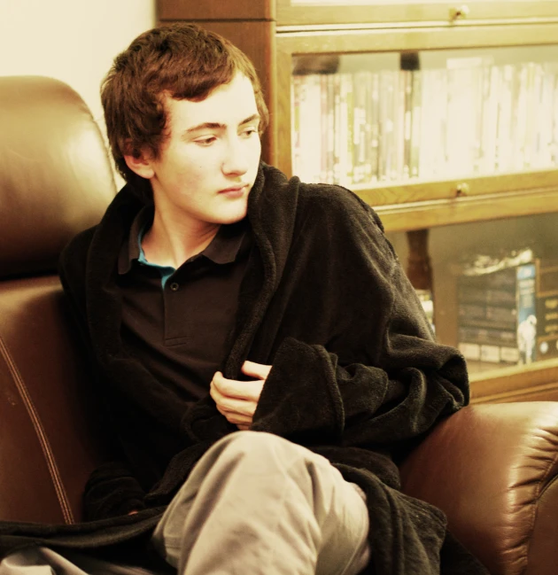 young man wearing black jacket sitting in chair with his hands crossed