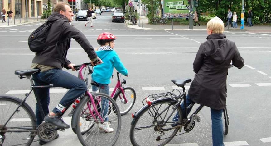 a woman, man, and little girl riding bikes across the street