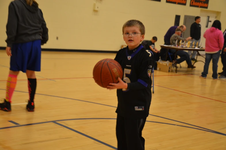 a small boy holds up a basketball in a gymnasium