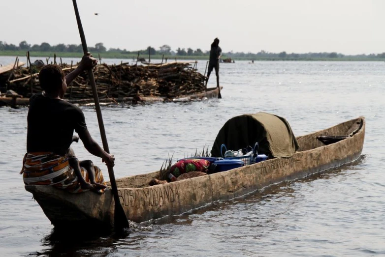 man standing on the edge of a long boat filled with items