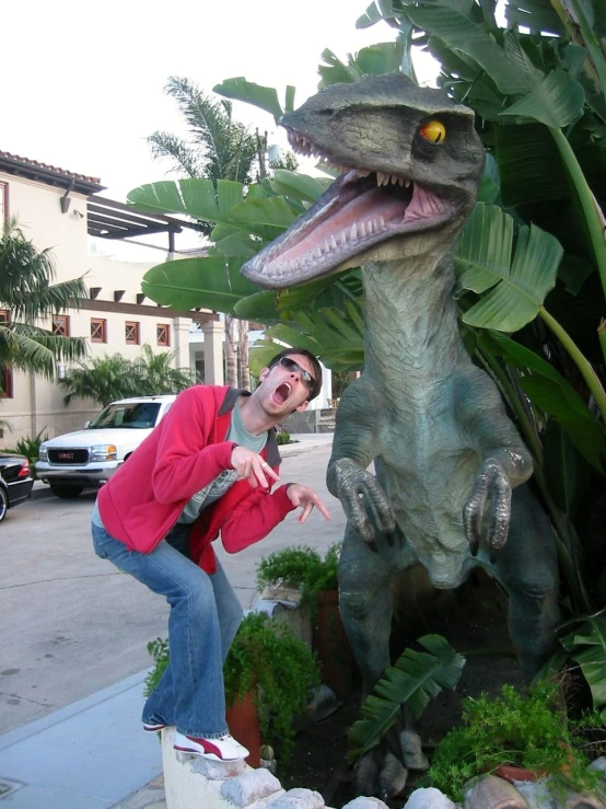 a man kneeling down in front of a fake dinosaur