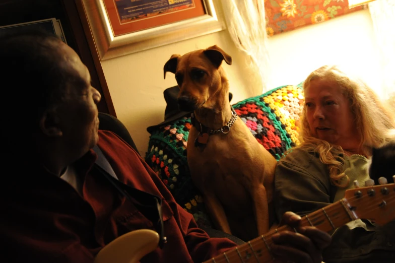 two people sitting on a couch while a dog watches