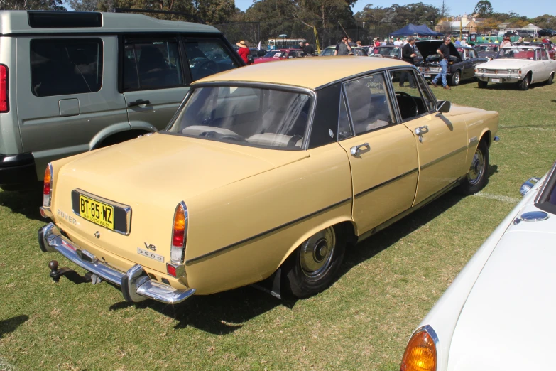 an old yellow car is parked on some grass