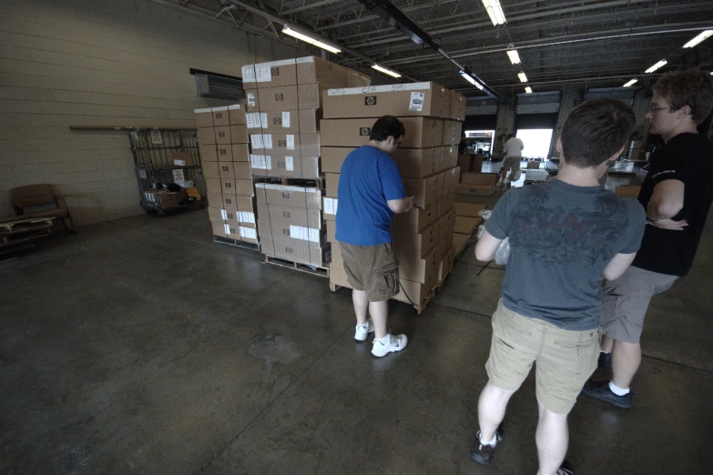 four people in warehouse with large stacks of cardboard boxes