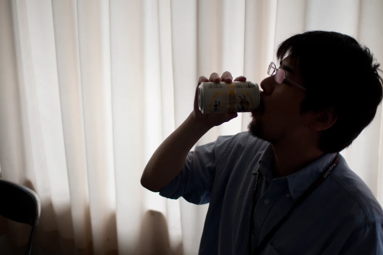 a man drinking from a tall canister in front of white curtains