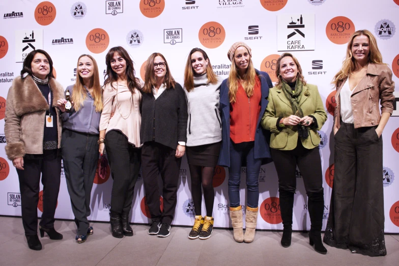 seven women standing on a red carpet with their hands together