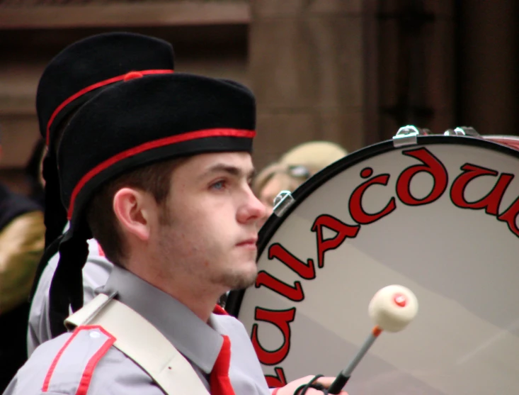 drummer looking on while wearing hat and playing a large drum