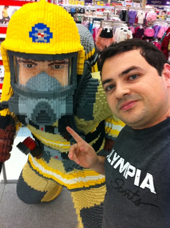 a man in grey shirt and yellow helmet standing next to a lego robot