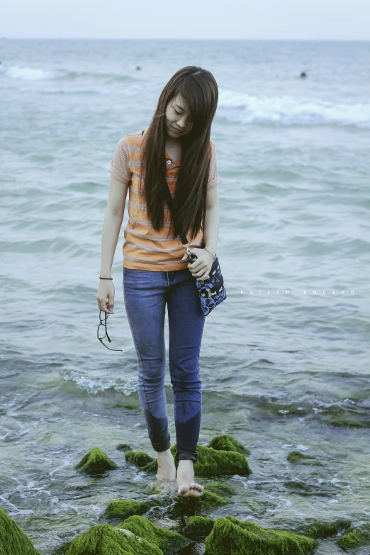 a girl wearing tight pants and a shirt standing on rocks by the ocean