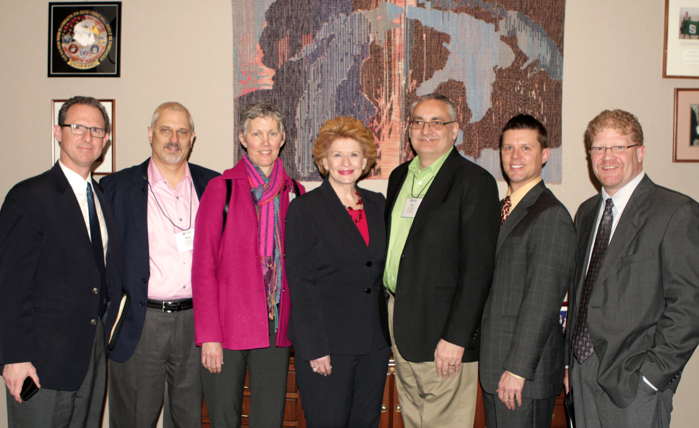 six people smiling for the camera in front of paintings