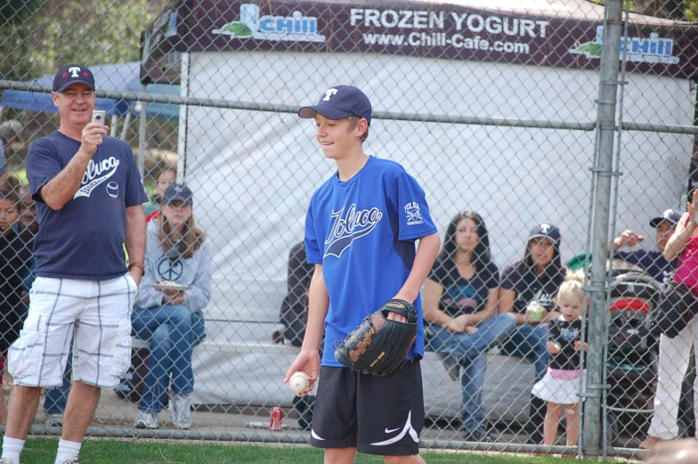 two s wearing baseball gloves in front of a fence