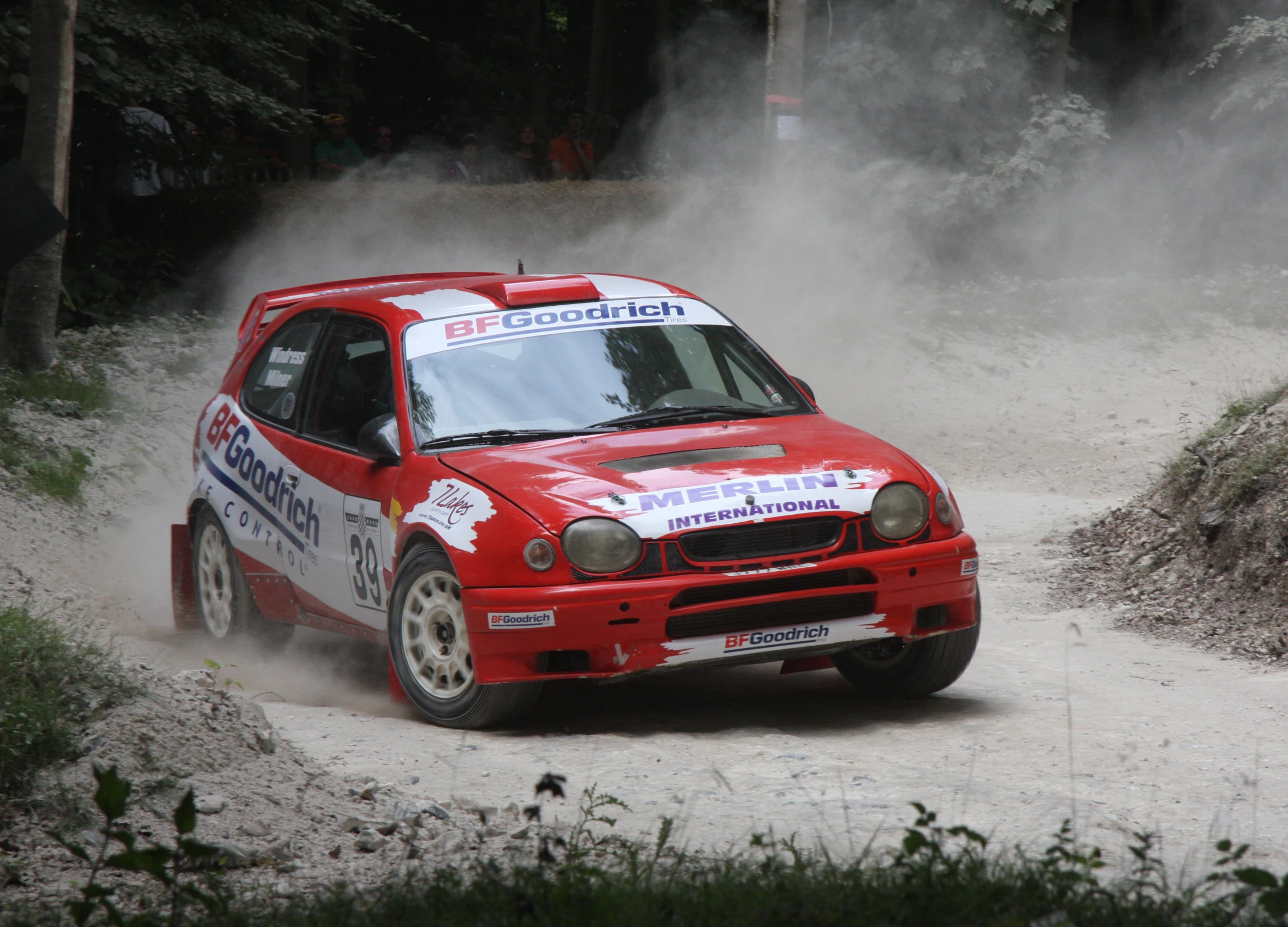 a red car driving through a dust covered forest