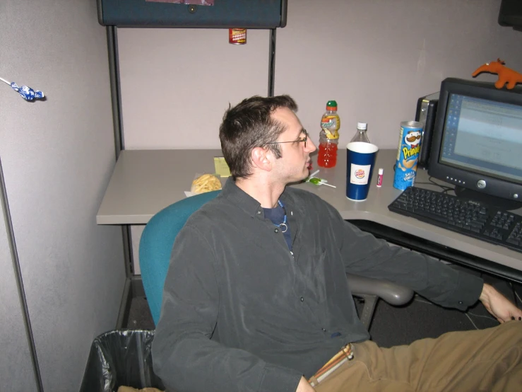 a man with glasses sitting at a desk looking at a monitor