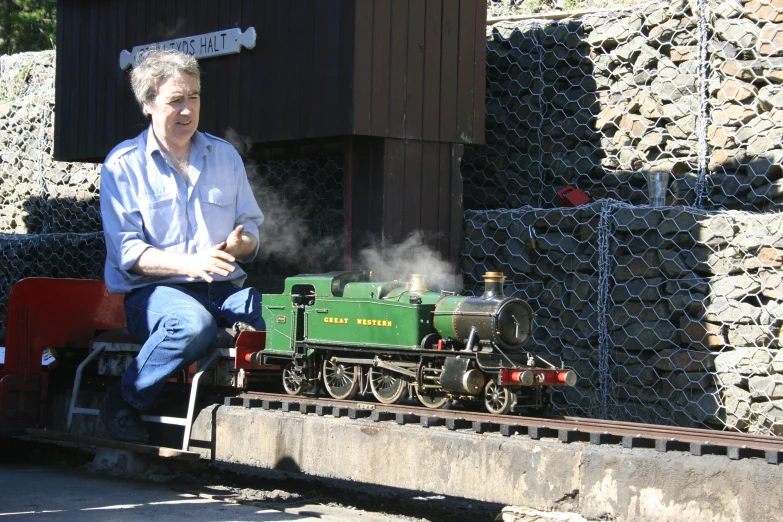 a man sits on a miniature train in front of a wooden building