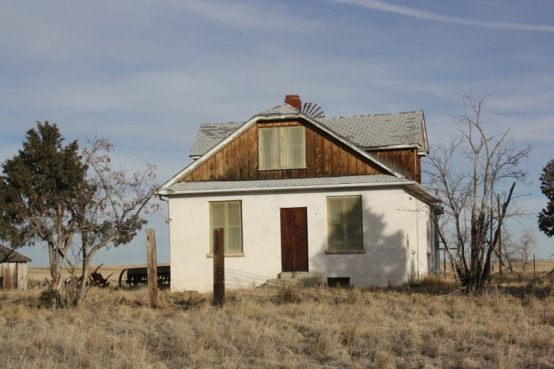 an old white house on a farm field with a cow in the yard