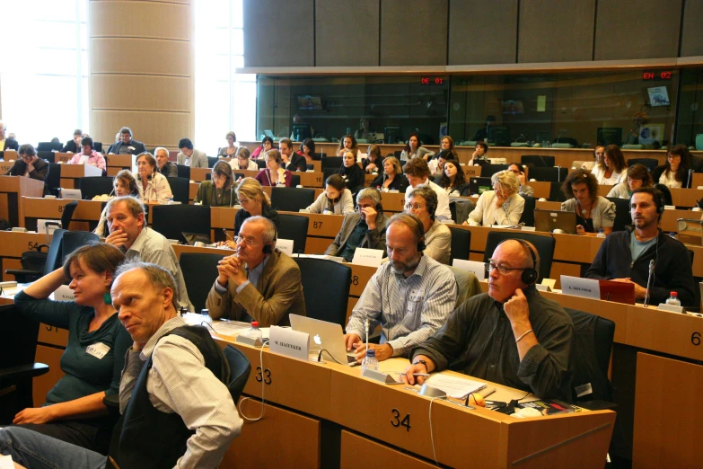 a group of people sitting at desks in a room with paper work