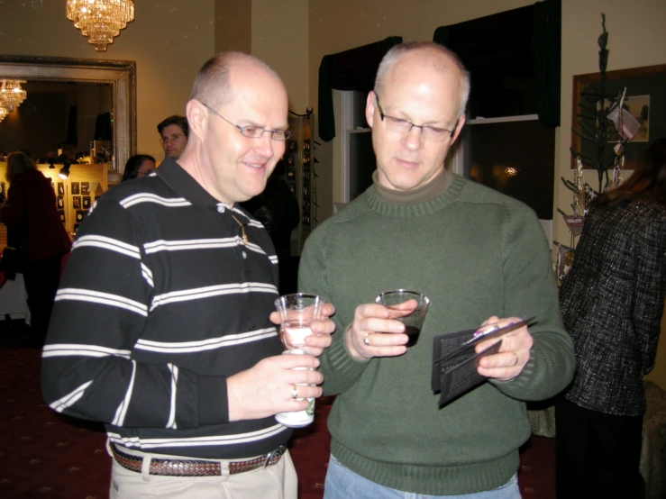 two men stand at a party, one holding drinks