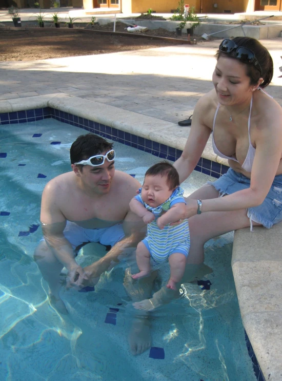 a woman and man with sunglasses and baby sitting in the water