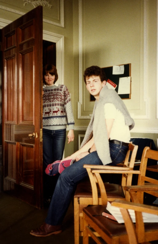 a young man and woman sitting down at a wooden table