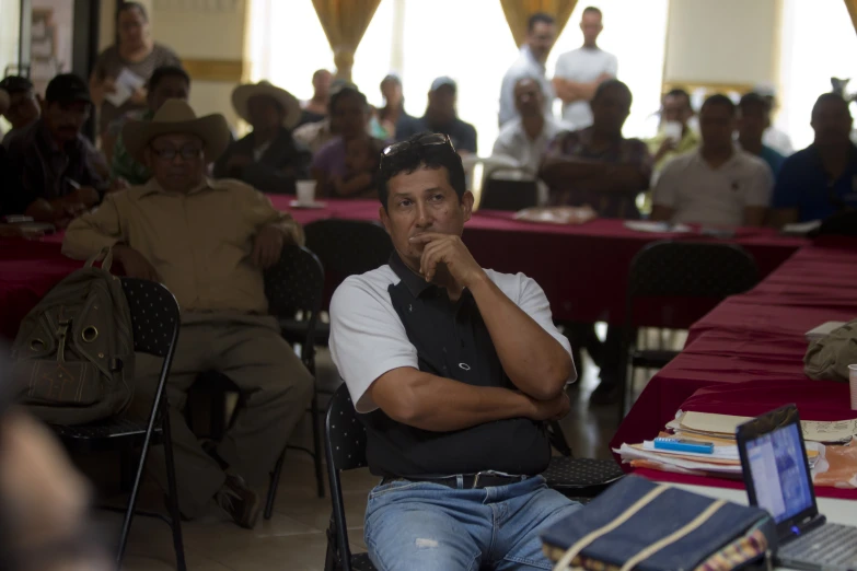 many people sitting down at long tables and there is a man on the laptop