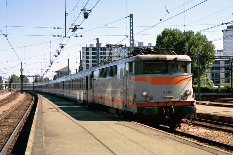 a silver and orange train traveling down tracks