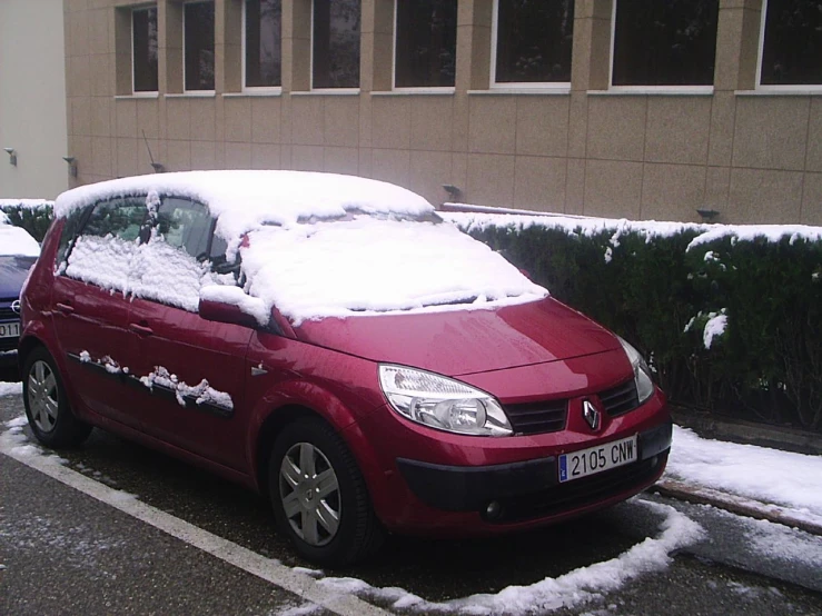 a maroon car is covered with snow in front of a beige building