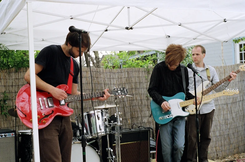 three men are playing guitar in front of a tent