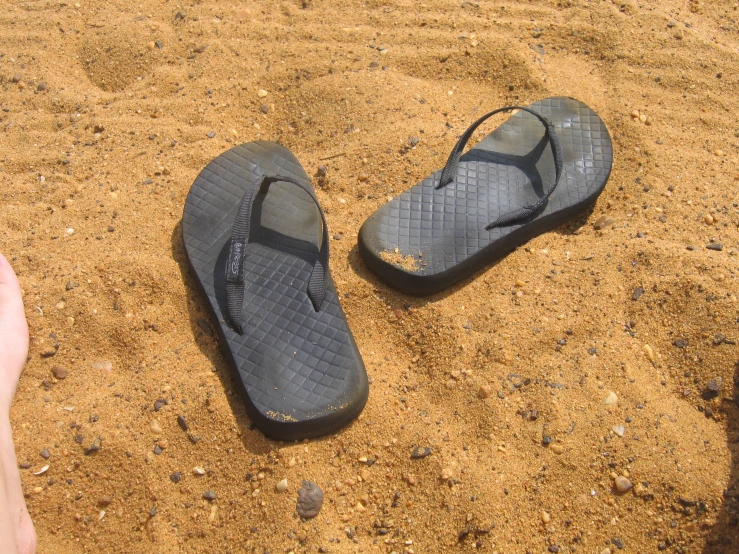 a pair of black shoes sit on the sand by a foot