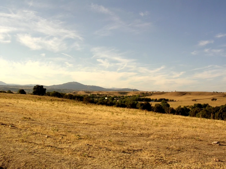 a hill covered in dry grass surrounded by hills