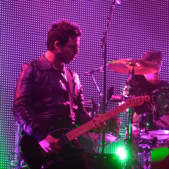 two people playing guitars in front of purple and green lights