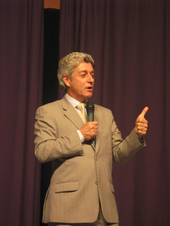 a man speaking at a microphone in front of purple curtains