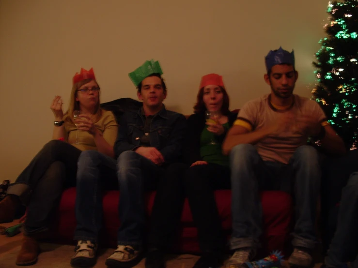 four people sit on a couch in front of a christmas tree